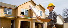photo of construction man looking at blueprint in front of home under construction